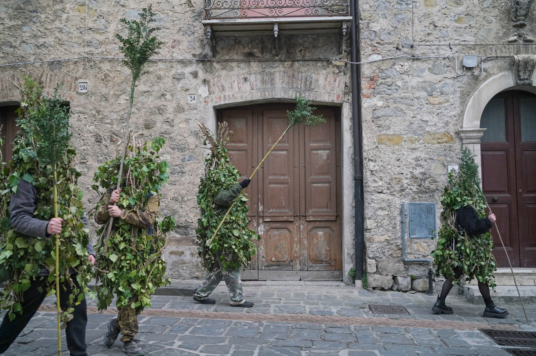 A photograph of four men walking while wearing “Rumita” outfits (made from tree branches) during a procession through the streets of Satriano.