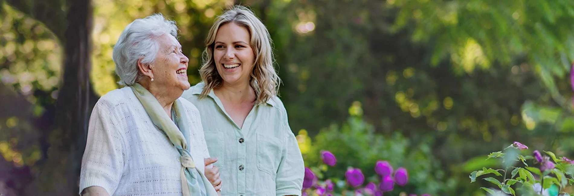 Two women walk together in a colorful garden.