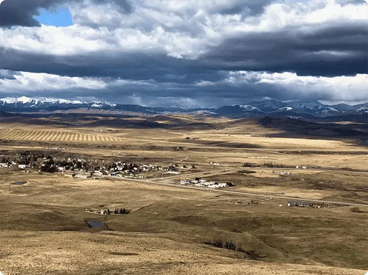 Aerial view of Alberta’s Eden Valley, a small community surrounded by hills with the Rocky Mountains in the distance.