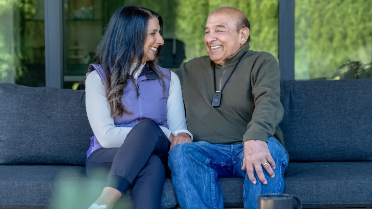 a younger women locking arms and smiling with an elderly woman who is wearing a medical alert system