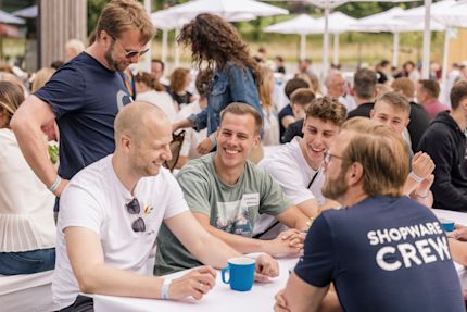 Eine Gruppe von shopware Mitarbeitern sitzt im Freien an einem Tisch und lächelt.