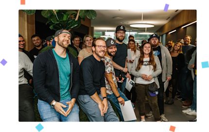 Shopware employees are gathered in the canteen and laughing together. The picture is surrounded by colorful confetti.