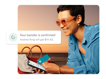 Woman on the beach looking at his mobile and holding and N26 You card. In the foreground there is a notification of an cross-border payment.