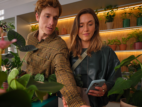 A man and a woman in a plant shop, with the woman holding a phone.