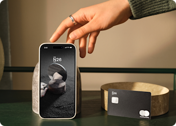 Hand reaching for a mobile standing on a table next to an N26 metal card.