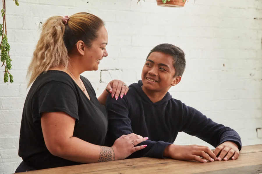 Mum casually resting her hands on her teenage son's arm as he sits at the kitchen counter.