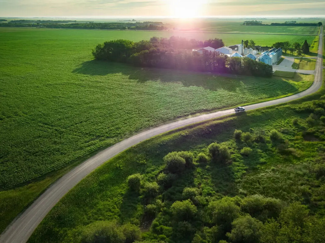 An aerial perspective of a farm and a car traveling on a country road, highlighting agricultural retail and crop planning.