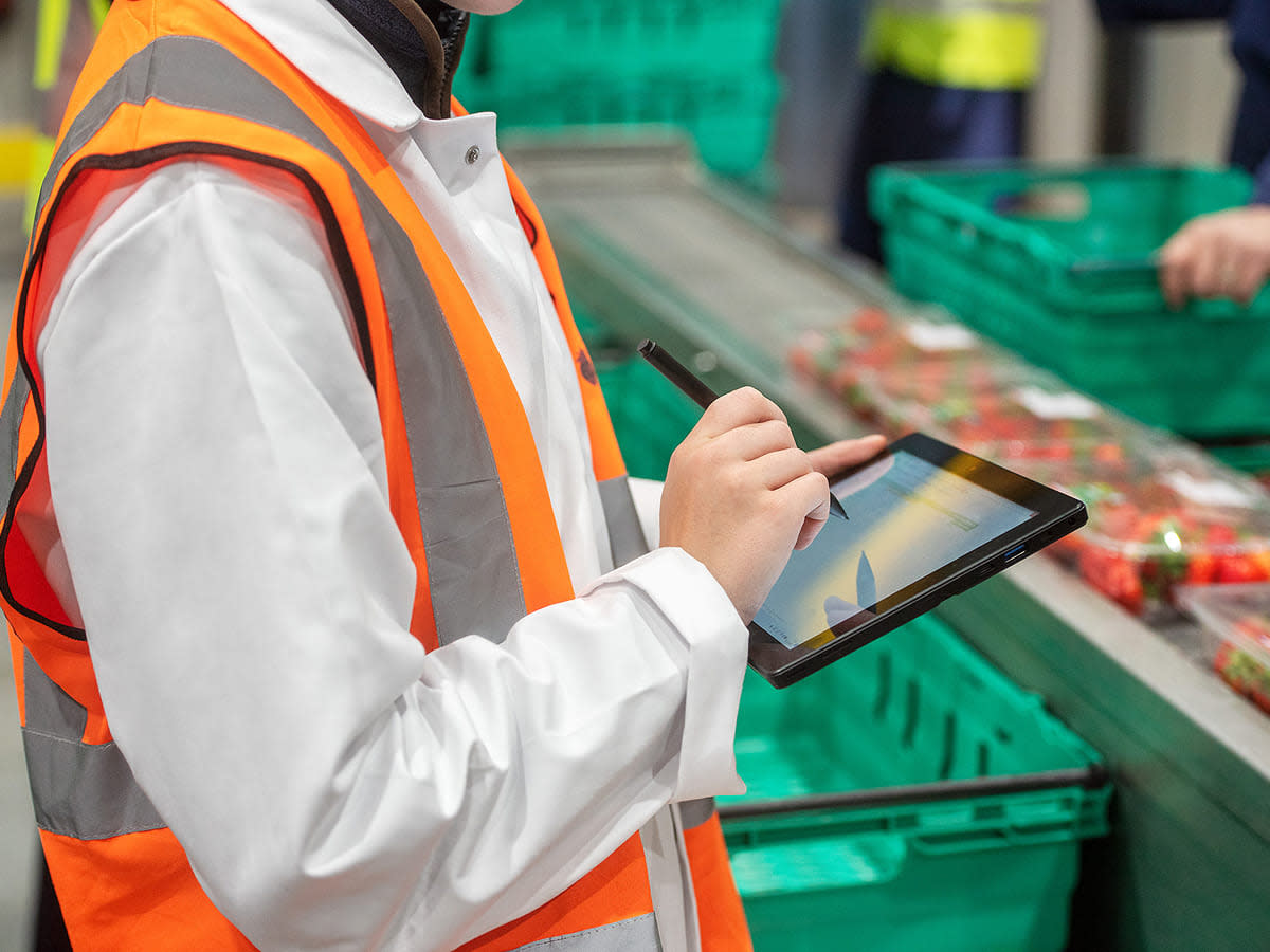 A person holding a tablet displaying a bar chart related to food safety and quality management software.